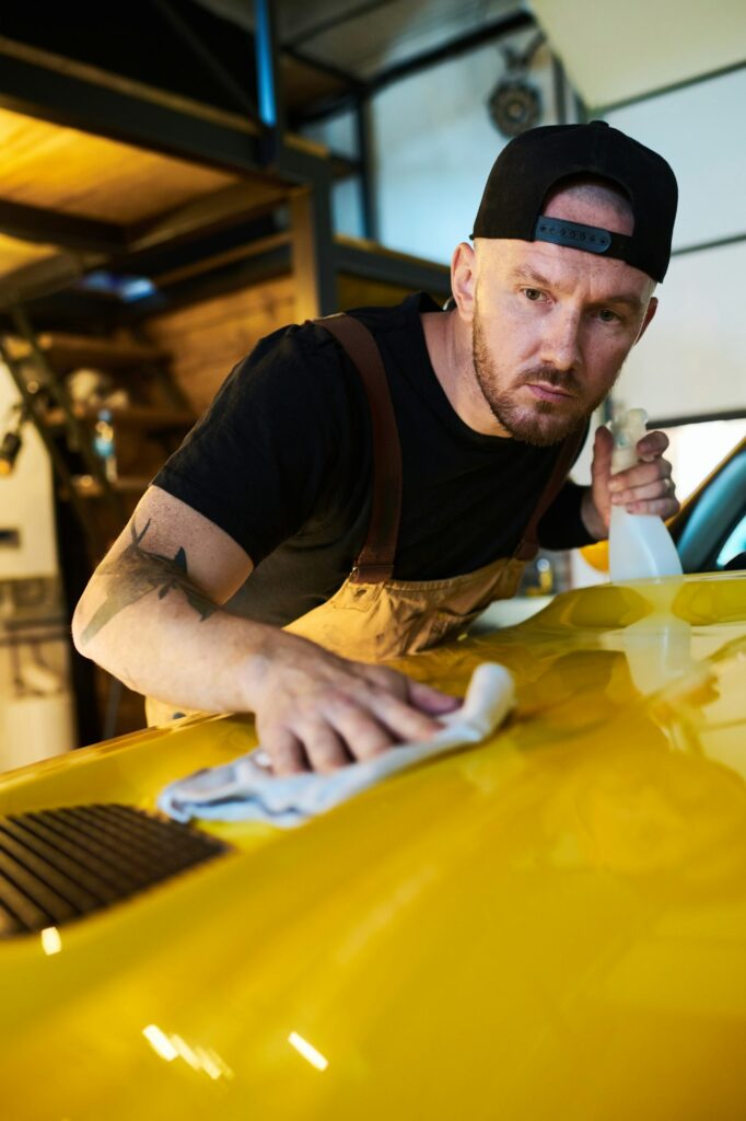 Young mechanic or technician of maintenance service cleaning cover of hood